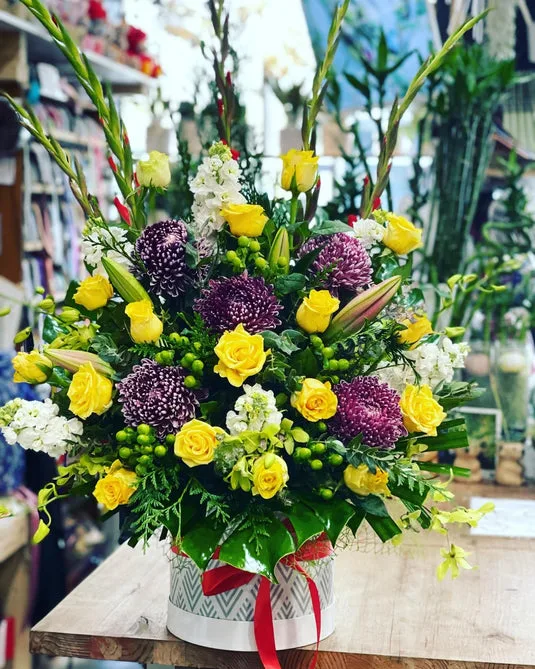 Yellow rose, purple chrysanthemum and gladioli arrangement in a patterned hatbox inside the shop