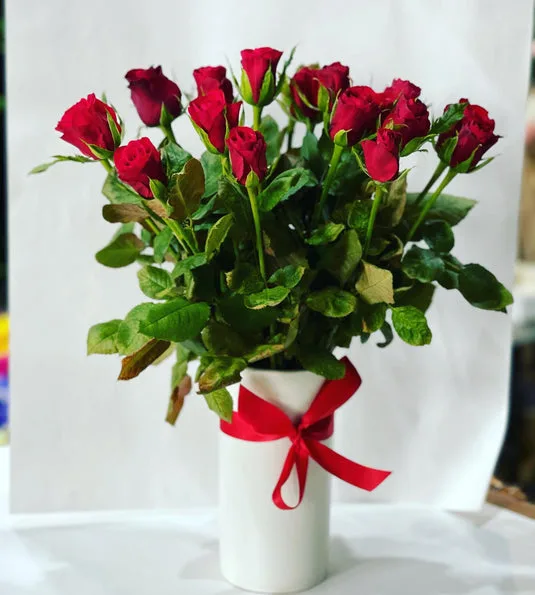 Red roses in a white cylinder vase with red ribbon