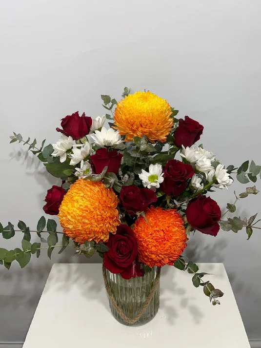 Orange chrysanthemum, red roses and eucalyptus in ribbed glass vase